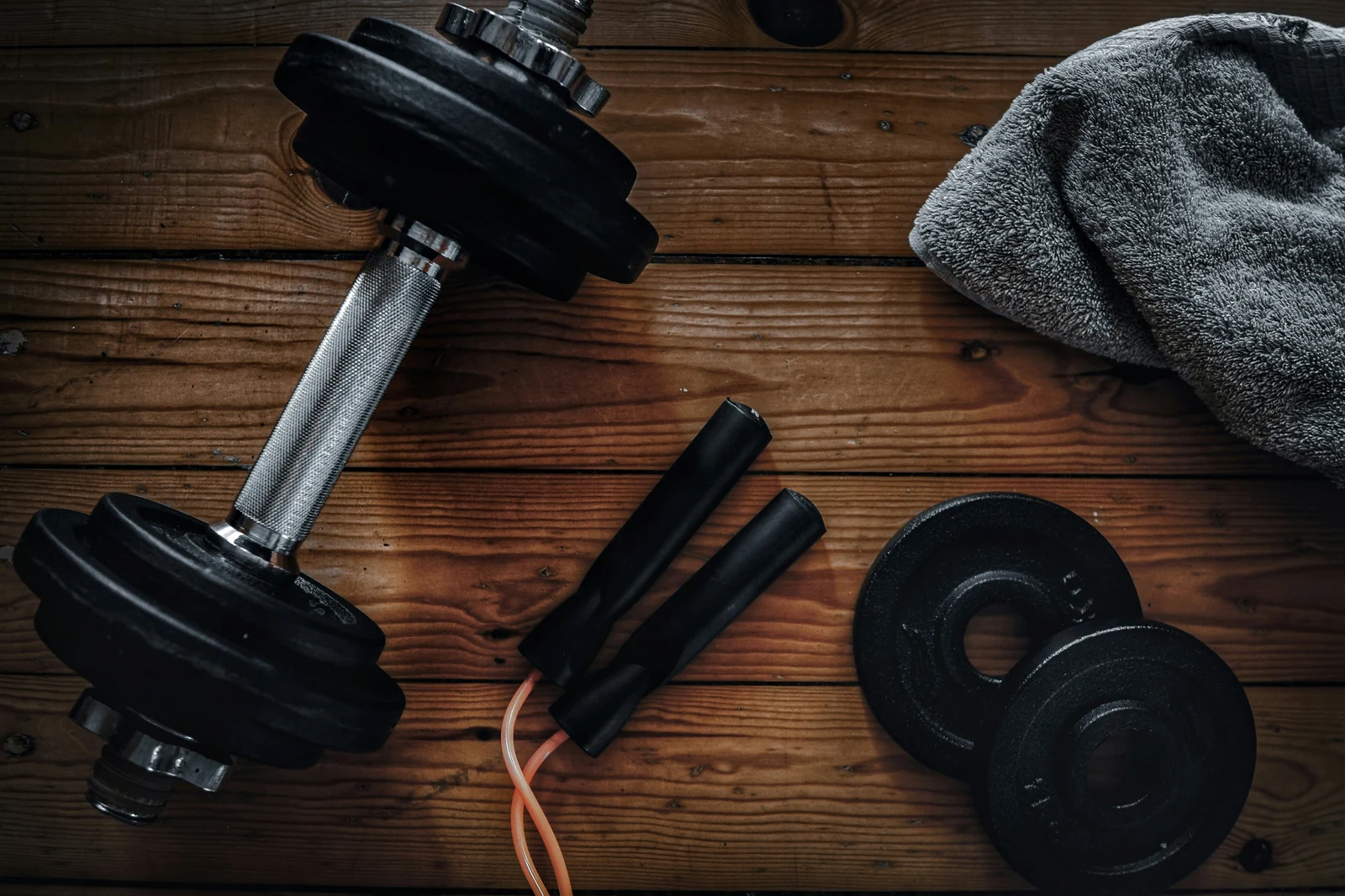 Dumbbells and a jump rope on a wooden training surface.